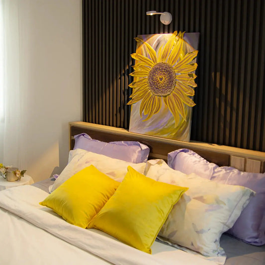 Bed with yellow and purple pillows and a sunflower decoration in the background.